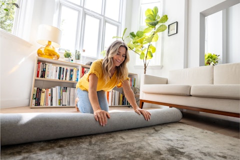 Happy Woman Moving House and Unrolling a Carpet While Unpacking