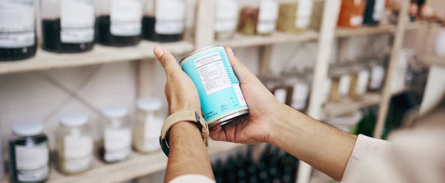 A person holding and reading the label on a packaged product inside a shop.