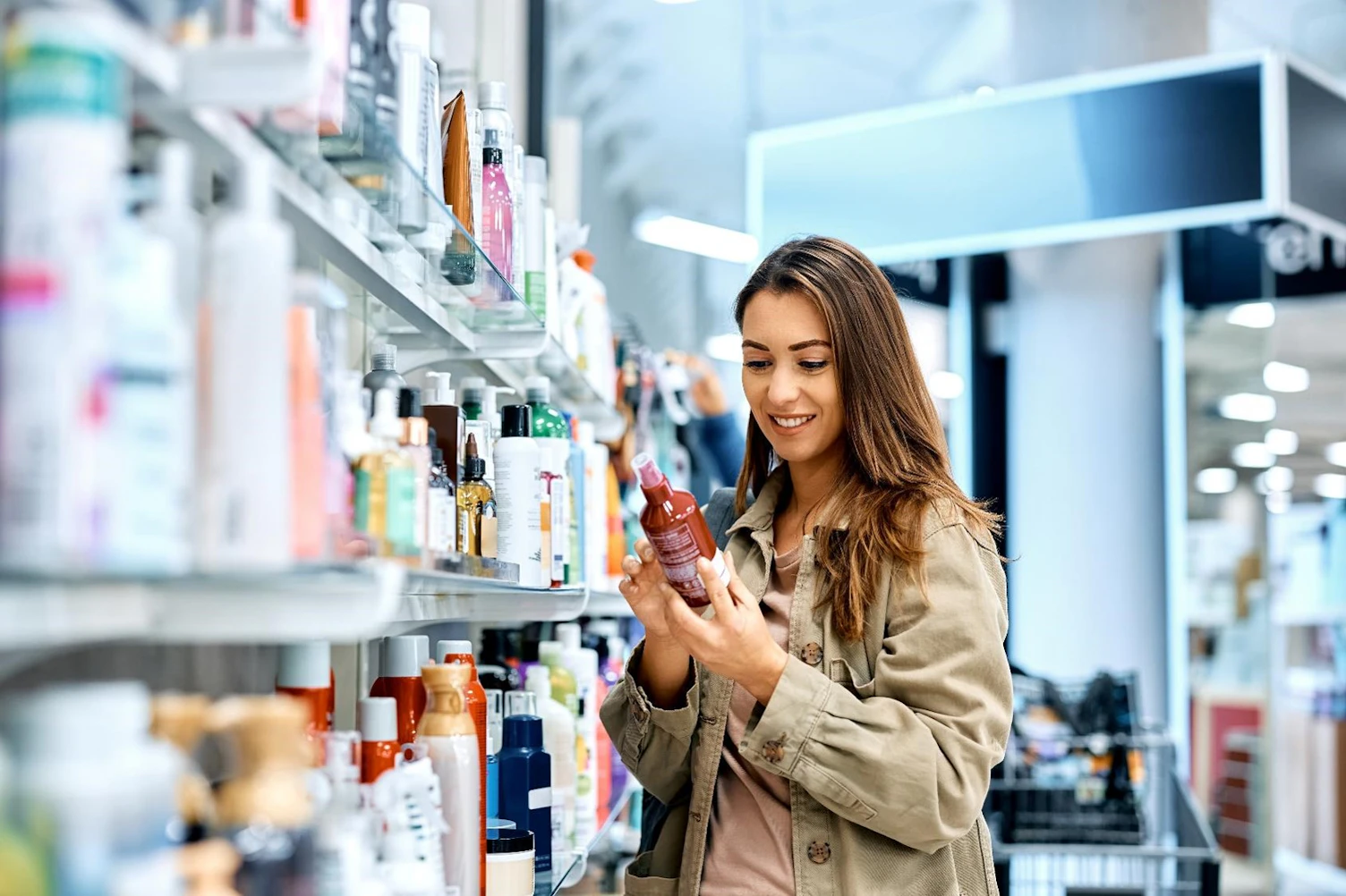 Young happy woman reading ingredients of skin care product while shopping at the store