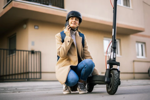 Young Woman Riding an Electric Scooter in the City Wearing a Helmet and Talking on her Smart Phone