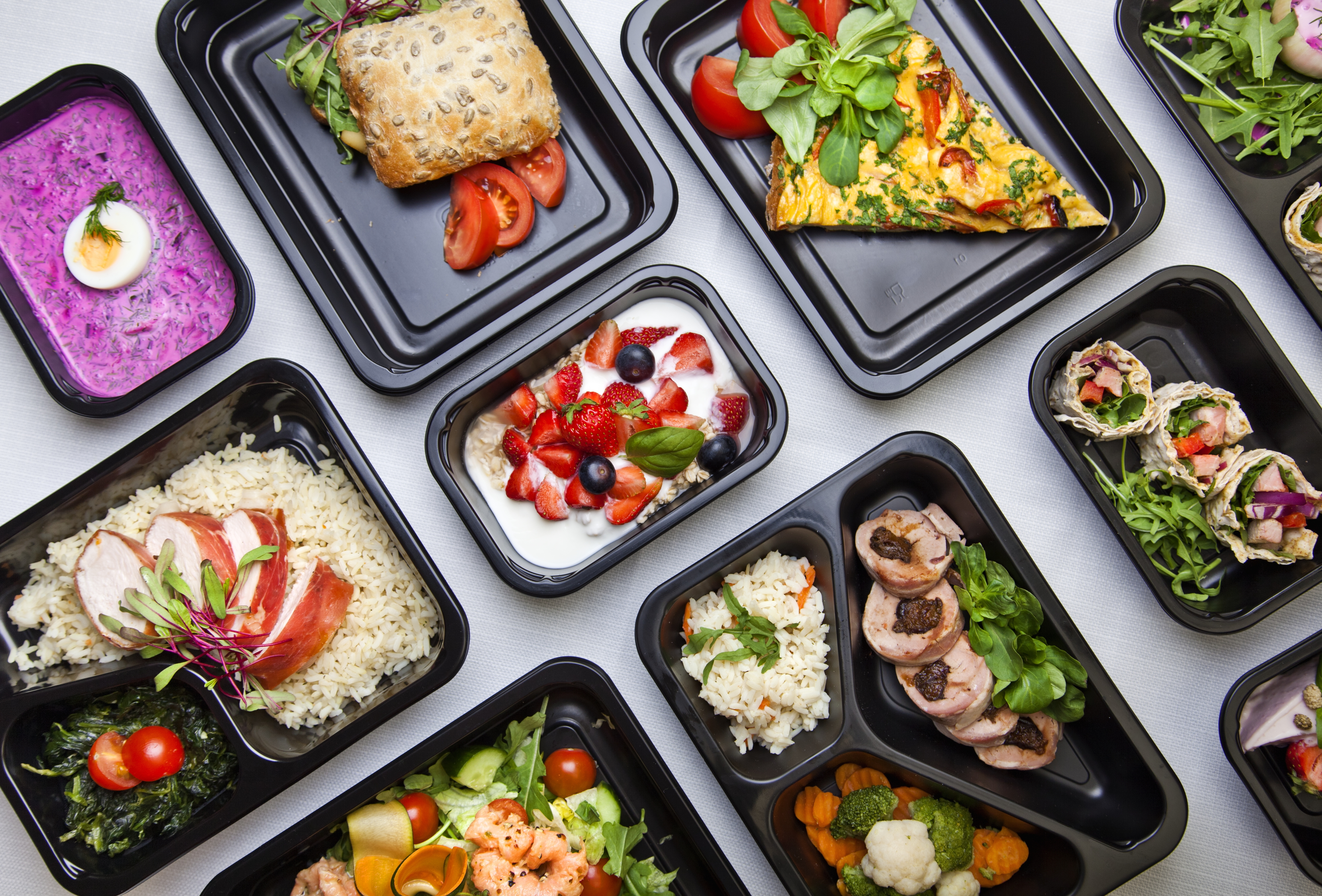 A variety of healthy, prepared meals neatly arranged in black takeaway containers