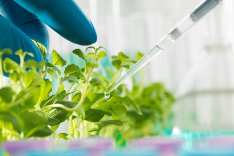 Gloved hand pipetting experimental chemical into laboratory seedling tray